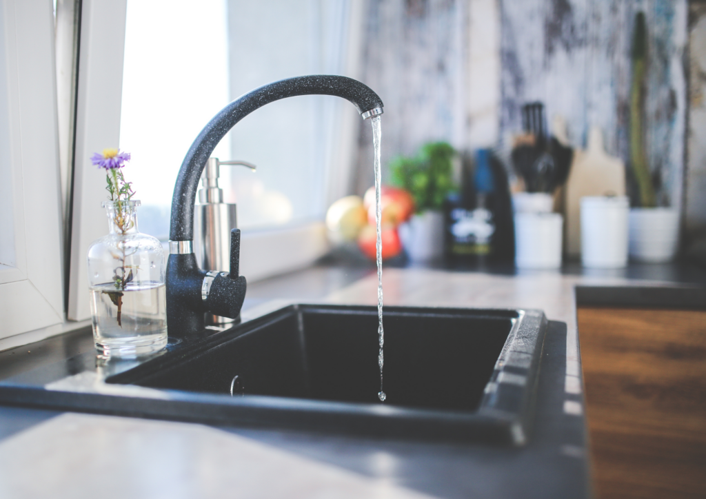 Robinetterie noire moderne avec eau coulante au-dessus d'un évier noir dans une cuisine contemporaine avec vue urbaine