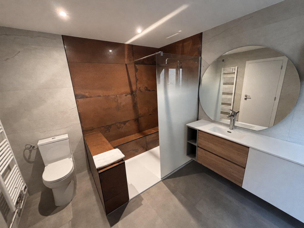 Salle de bain moderne avec douche à l'italienne aux carreaux couleur rouille, lavabo suspendu bois, miroir rond et toilettes